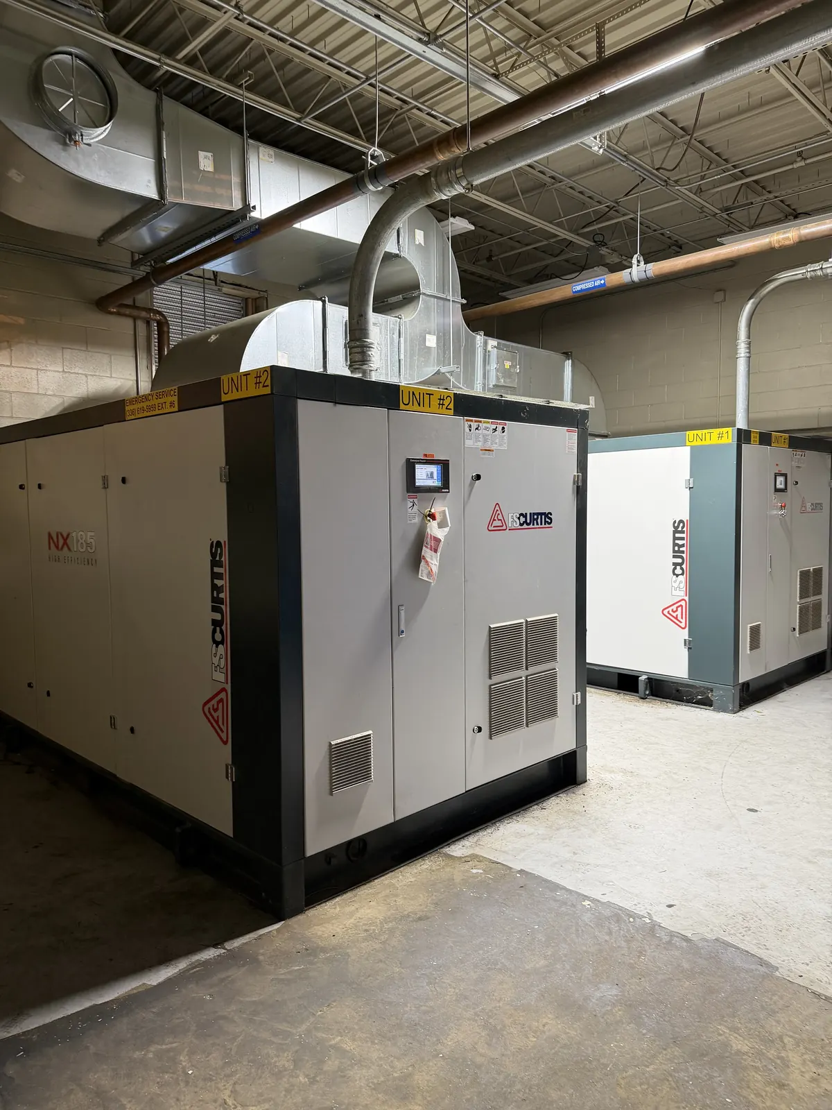 Two industrial air compressors set and wired by CDS in a plant compressor room