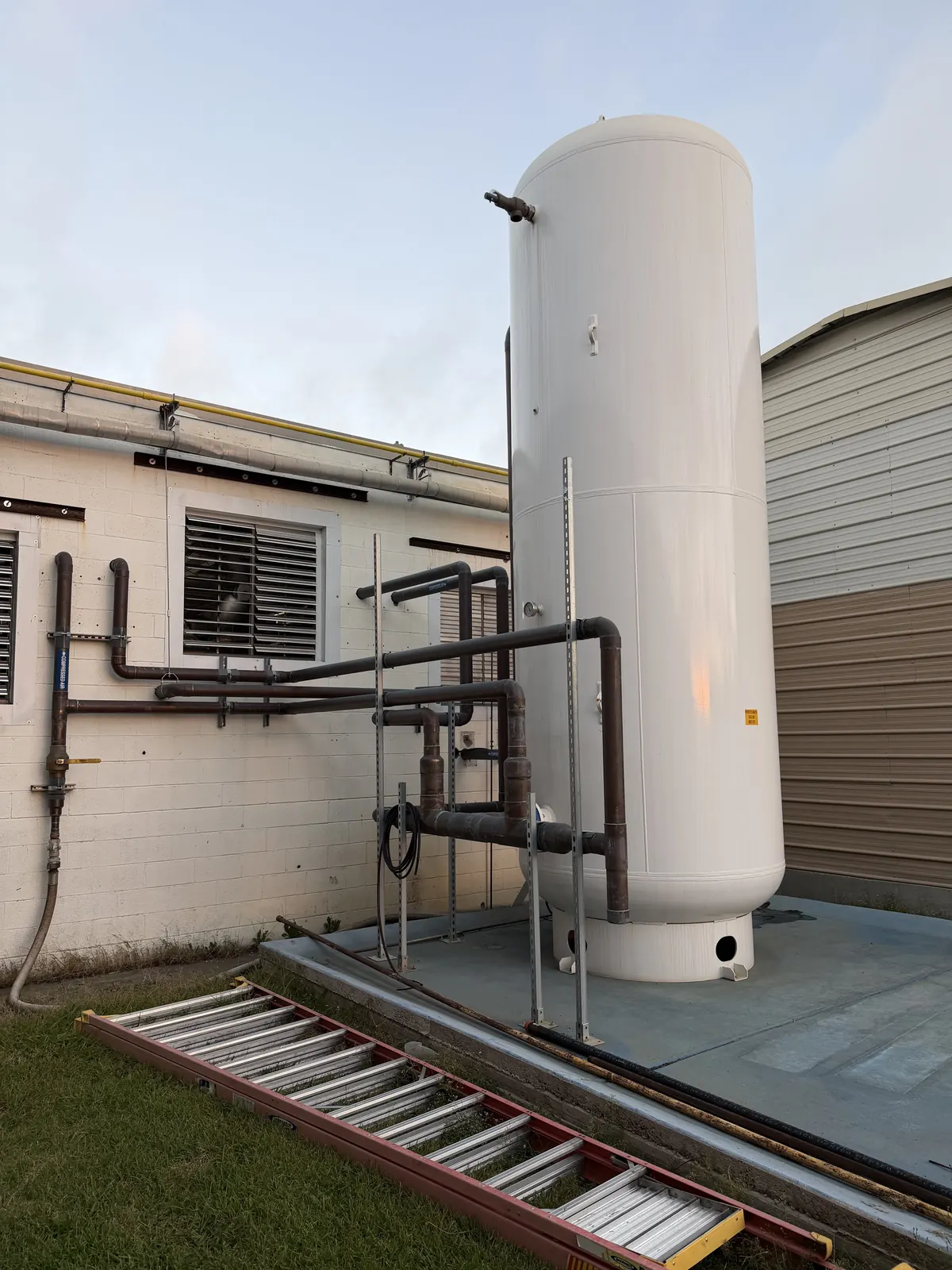 Tall outdoor air tank set by CDS beside a manufacturing plant