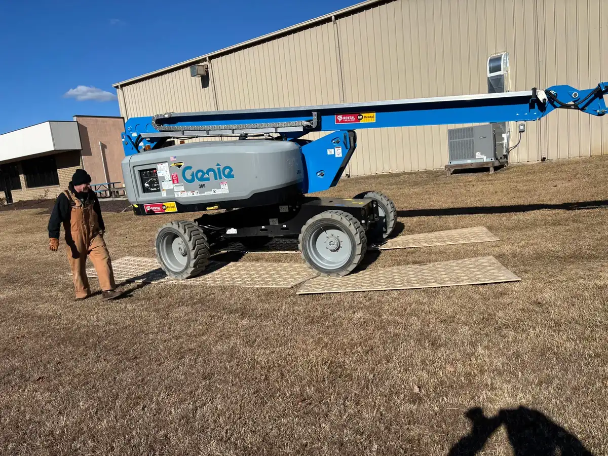 Crew member walking beside a boom lift at an industrial job site