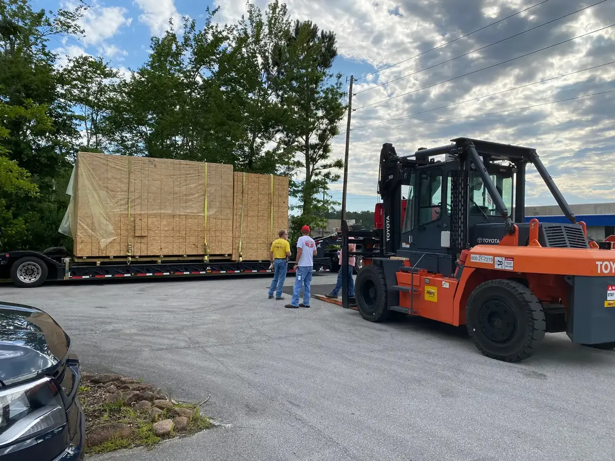 Forklift unloading a crated machine from a flatbed trailer
